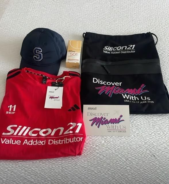 Silicon21 welcome kit laid out: red personalized jersey, monogrammed navy cap, SPF 50+ sunscreen, Discover Miami drawstring bag and welcome card